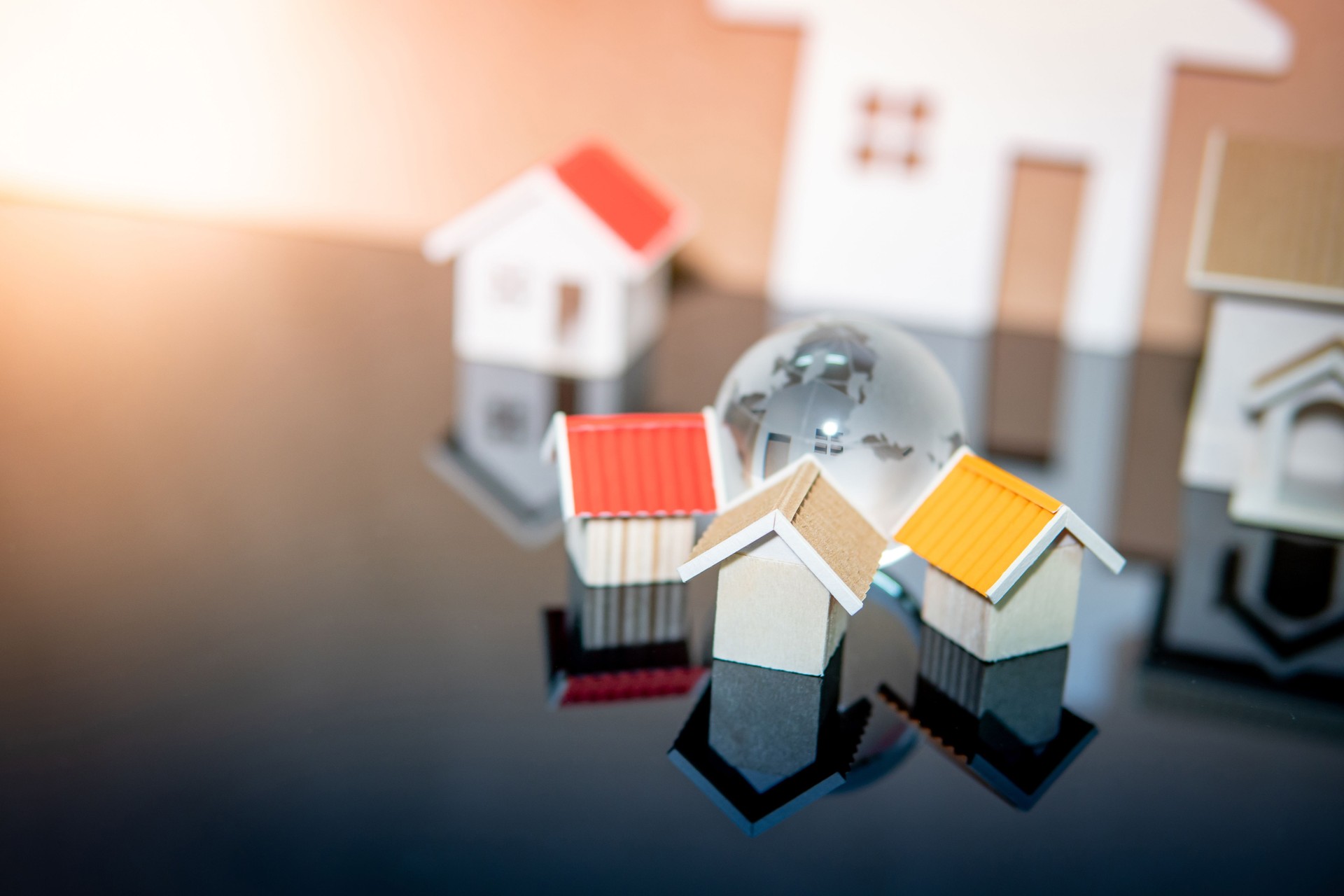 Global real estate or property investment concept. Wooden house models and world globe crystal glass on reflective table. Housing development business.